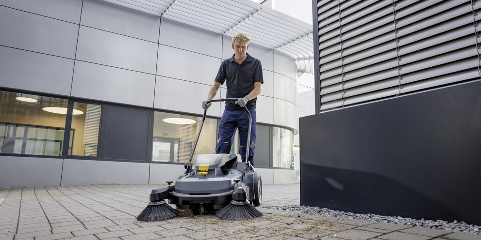 Green Space Maintenance & Outdoor Cleaning A worker uses a walk-behind sweeper to clean outdoor spaces