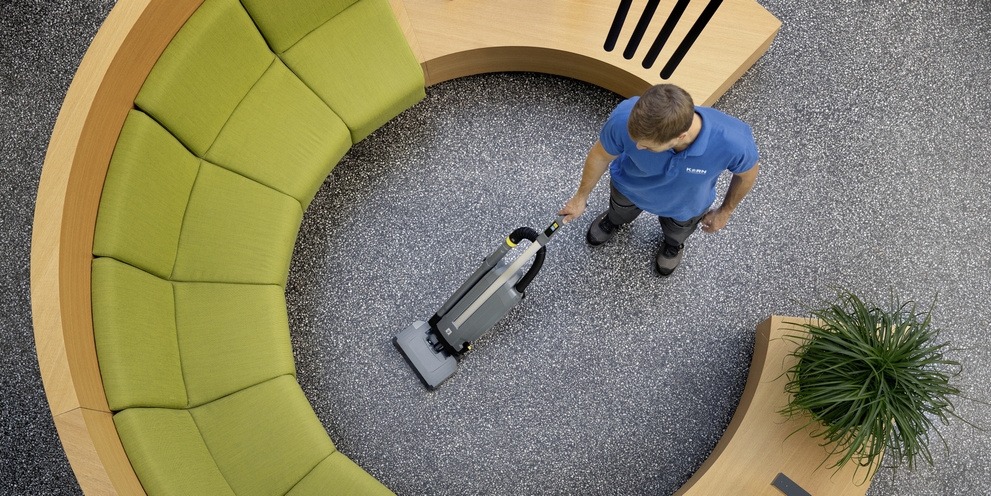 A person cleaning the carpet with an upright brush vacuum cleaner.