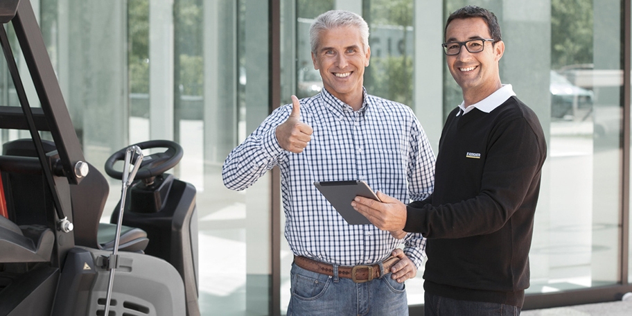 A man with a tablet smiles next to another man who gives a thumbs up.
