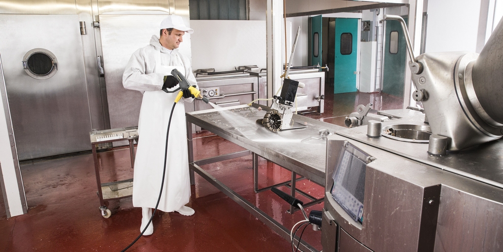 A worker pressure washes the work area inside a butcher shop.