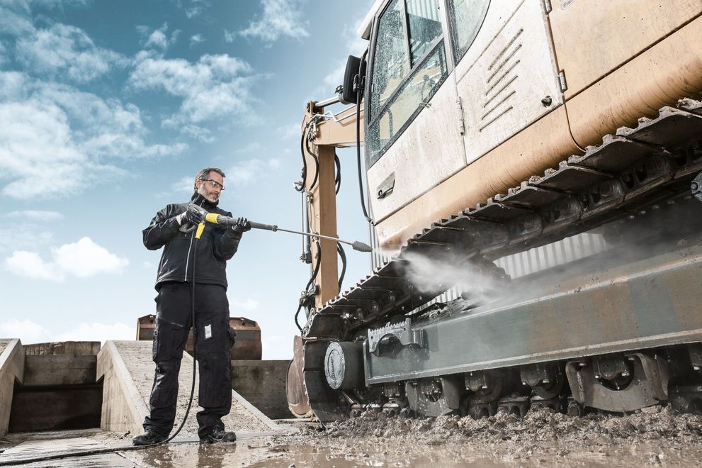 A worker uses a gas-powered hot water pressure washer to clean construction equipment.