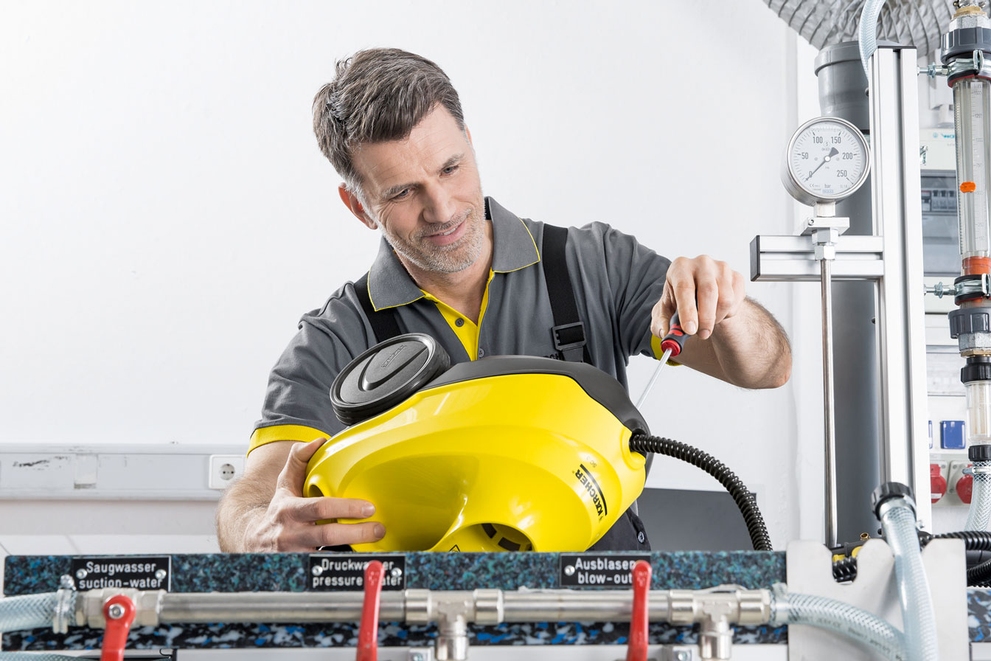 A service technician repairs a yellow Kärcher steam cleaner.