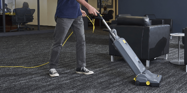 A worker uses a Kärcher stand-up vacuum in an office.