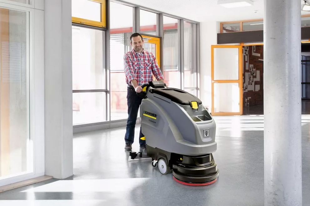 A worker cleans office floors with a walk-behind floor scrubber.