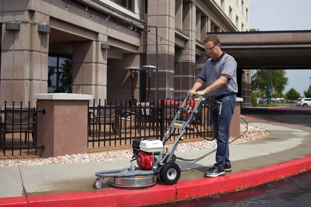 A worker uses a Jarvis Pressure Washer to clean sidewalks outside a hotel.