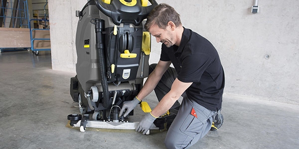 A Kärcher service technician adjusts a squeegee on a walk-behind floor scrubber.