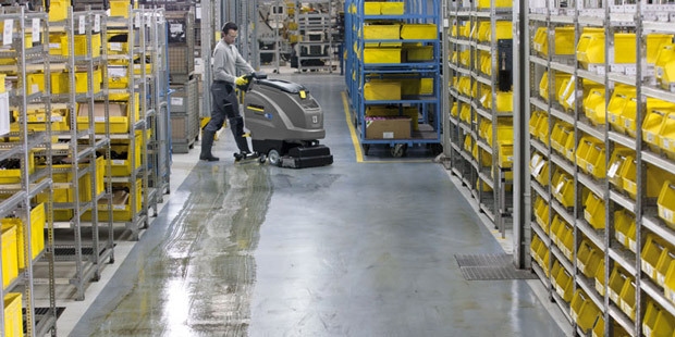 A worker cleans warehouse floors with building care detergents.