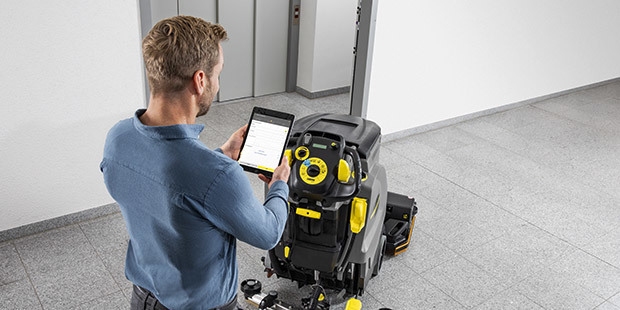 A man stands next to a floor scrubber holding a tablet.