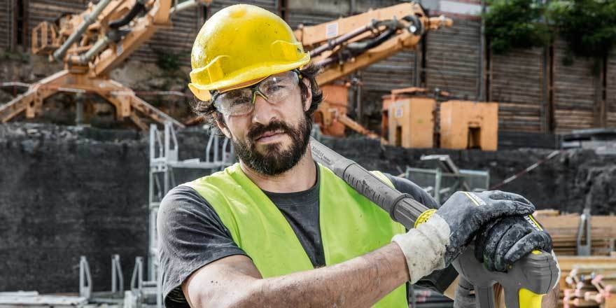 A construction worker carries a pressure washer lance over his shoulder.