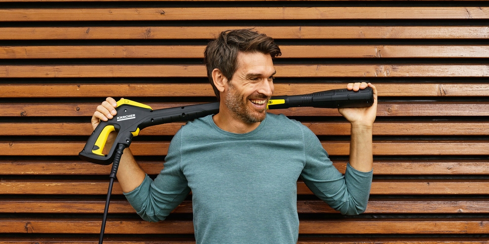 A man holds a pressure washer gun over his shoulder.