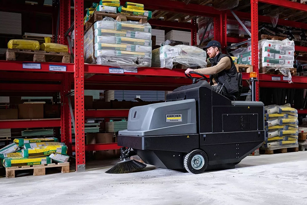 A worker uses a KM 105/180 Floor Sweeper to clean floors in an industrial environment.