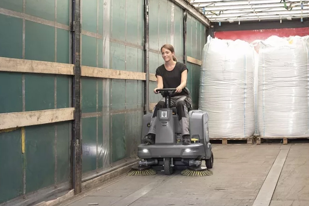 A worker uses a KM 85/50 Floor Sweeper to clean inside a shipping container.