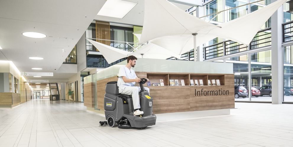 A person is sitting on a ride-on floor scrubber and cleaning the entrance area of a hospital