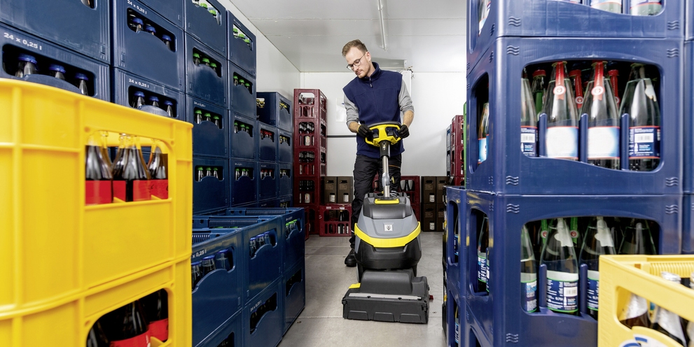 A worker uses floor cleaning equipment inside a walk-in cooler