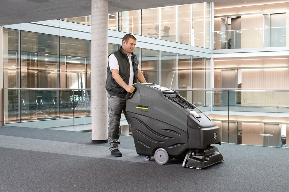 A worker uses a walk-behind extractor to clean office carpets.