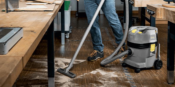 A worker using a vacuum to collect dirt off a hardwood floor.