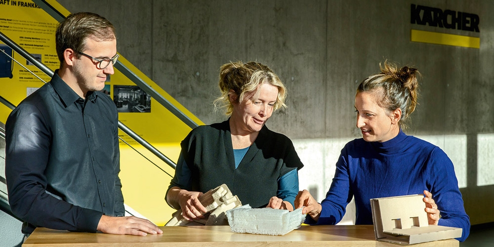 Three workers discuss cleaning solutions at a table.