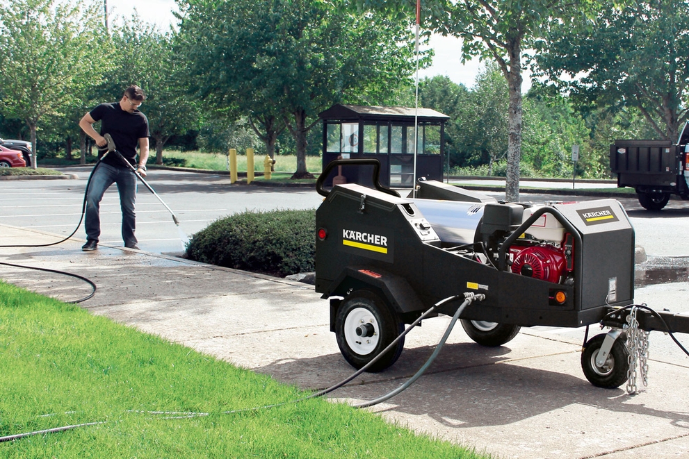 A worker cleans a parking lot using a pressure washer trailer.