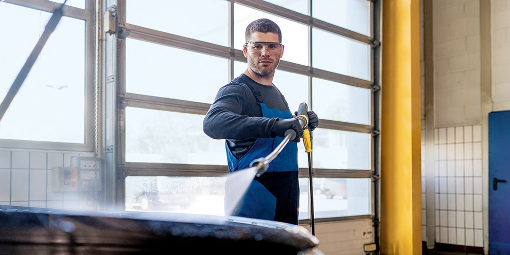 A worker pressure washes in a garage with an electric-powered machine.