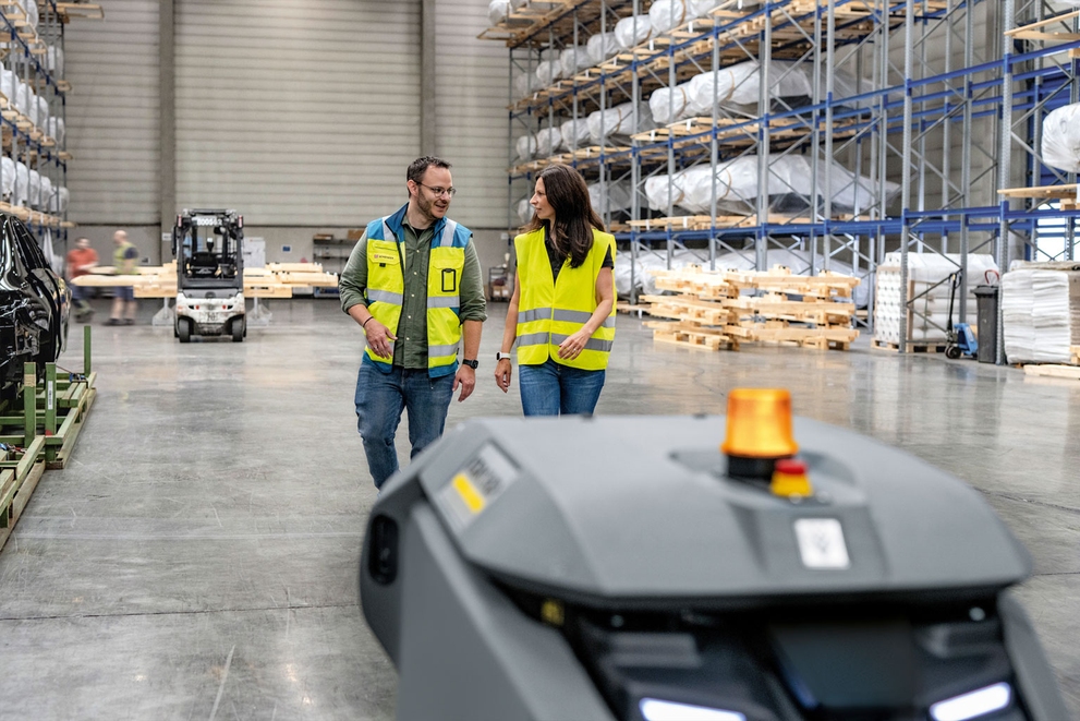 Return on Investment Two workers in a warehouse talk while a KIRA B 50 scrubs floors.