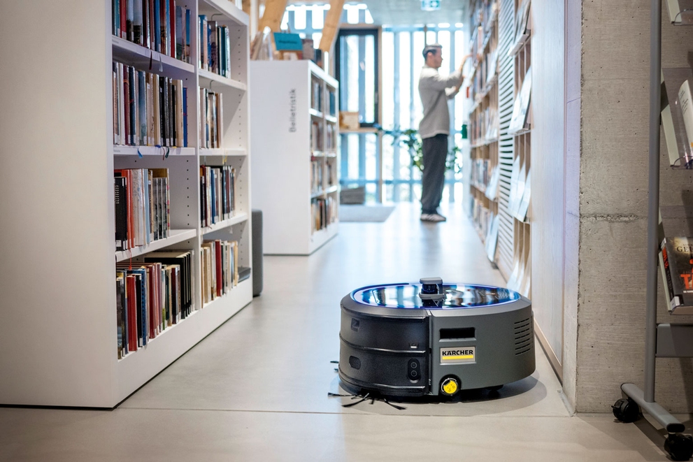 An autonomous vacuum cleans library floors while workers take care of other cleaning tasks.