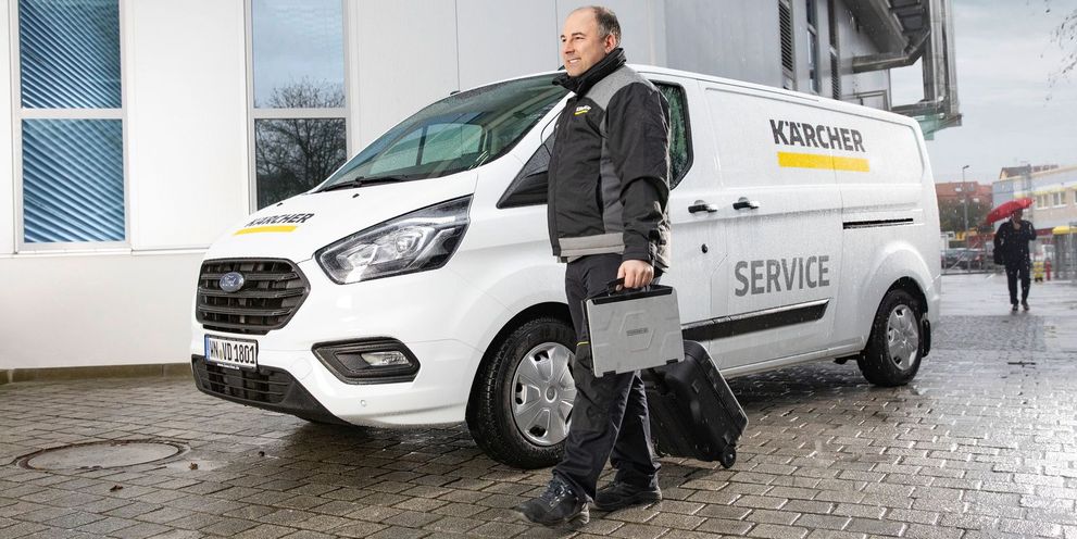 A Kärcher service technician carries a toolkit as he walks next to his service van.