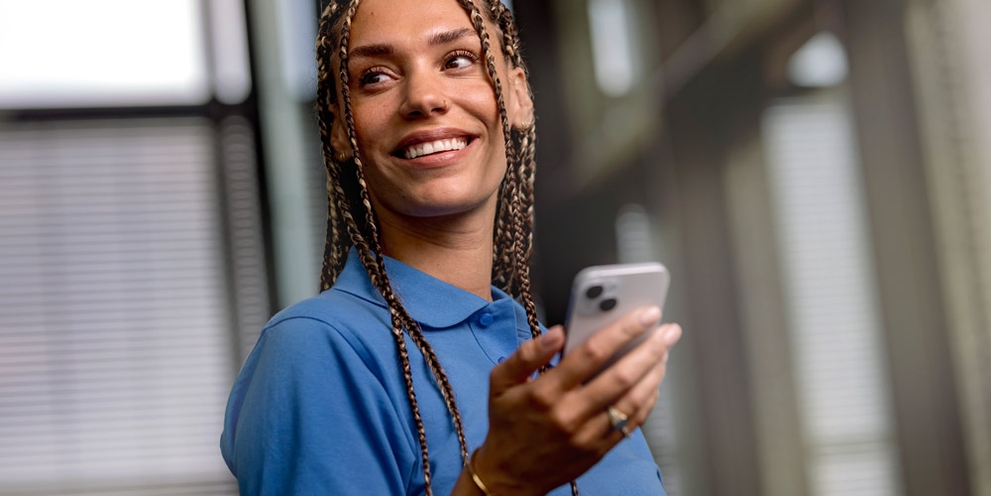 A woman smiles as she holds her smartphone.