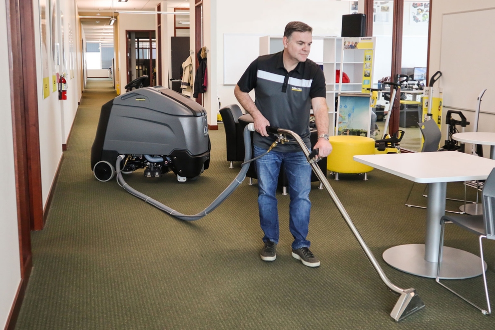A worker uses a stand-on extractor to clean office carpets.