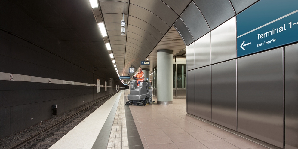 A person sits on a ride-on sweeper and cleans a platform