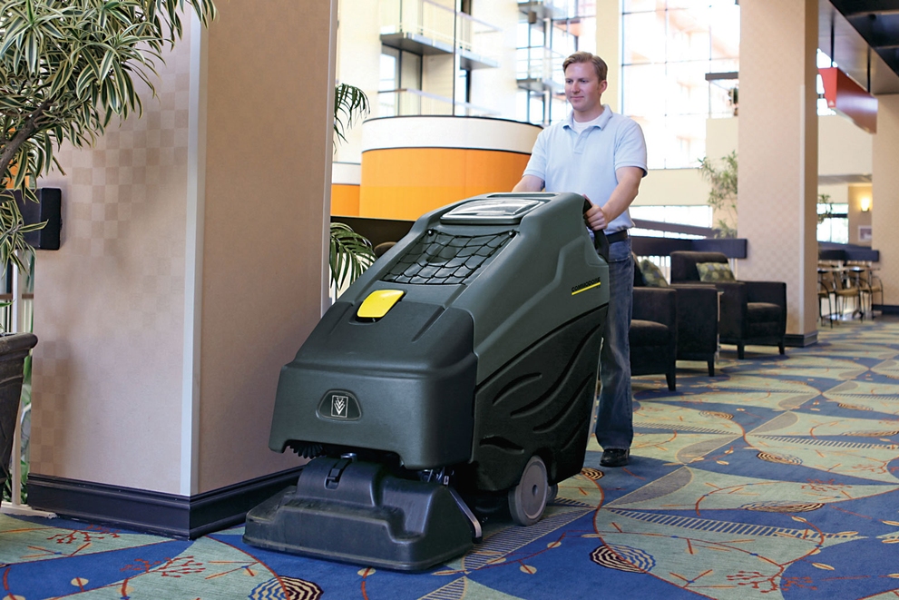 A worker cleans hotel lobby carpets using a walk-behind extractor.