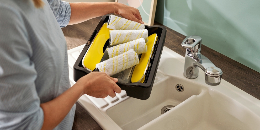 Person washes rollers of the floor cleaner