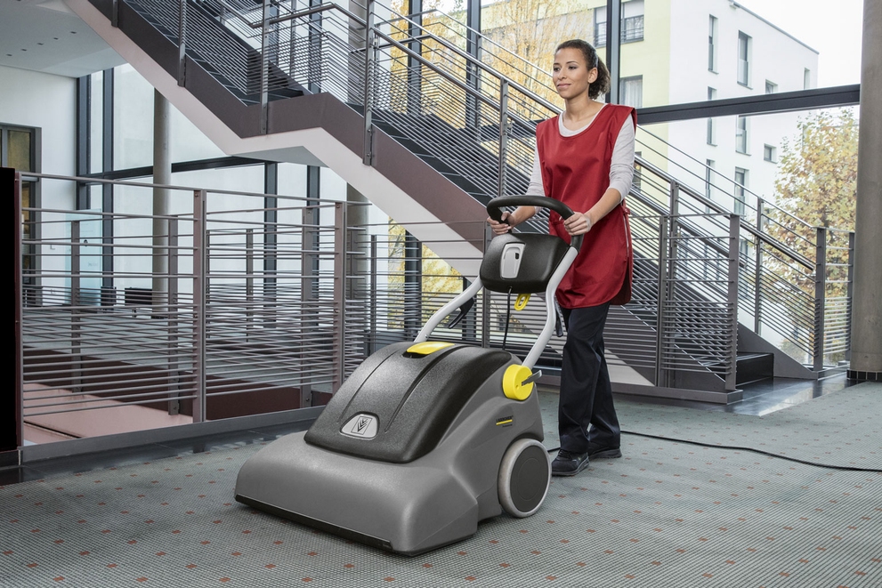A worker uses a wide-area vacuum to clean long hallway carpets.