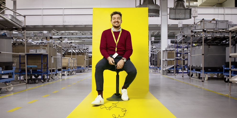 A Kärcher employee sits on a stool with a yellow backdrop inside the factory