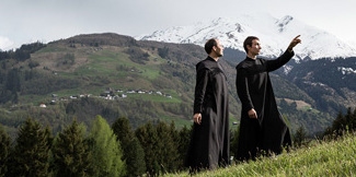 Two members of the Disentis monastery on a grass hill in Switzerland