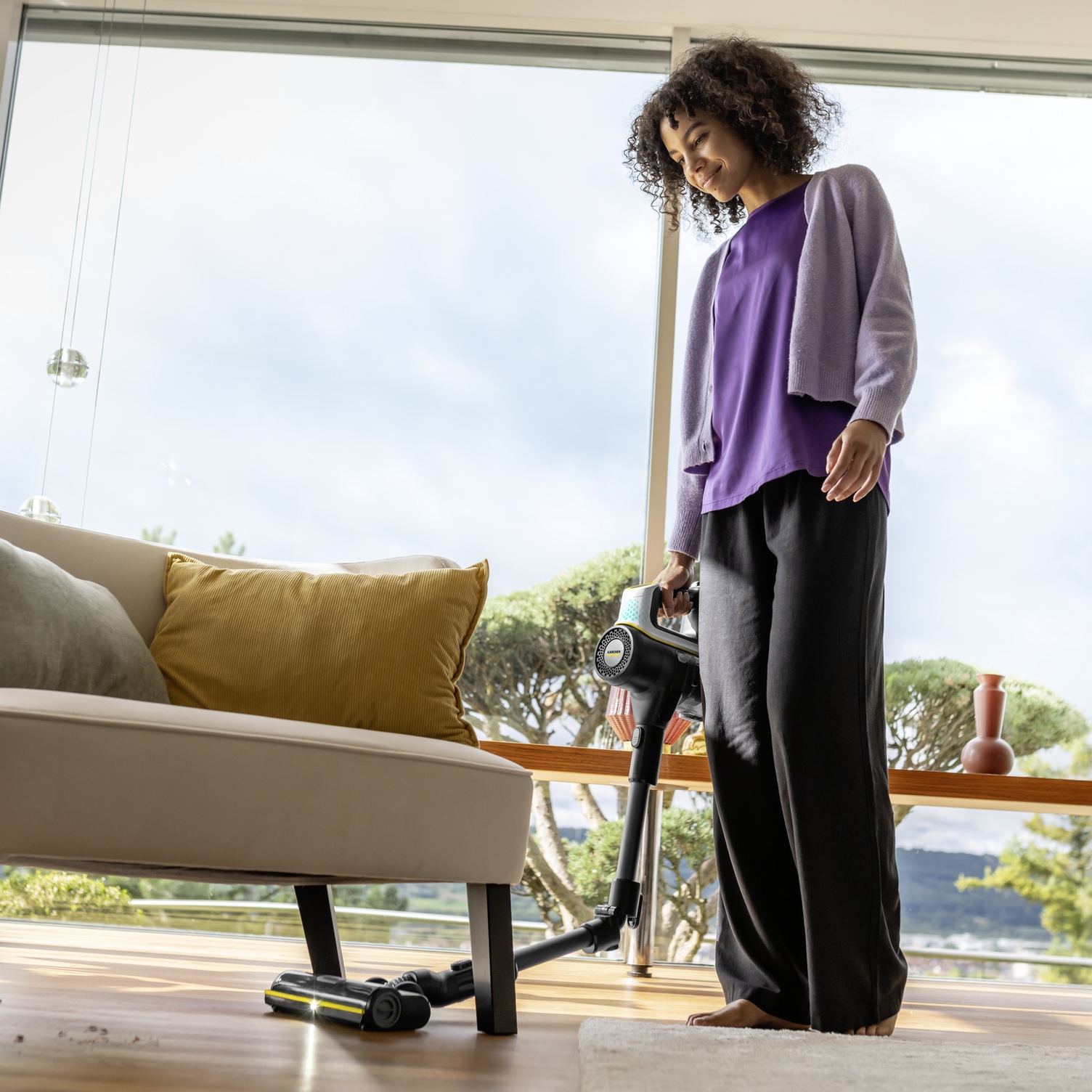 Flexible joint for maximum depth range Woman effortlessly vacuuming deep under a sofa with a Kärcher battery-powered vacuum cleaner thanks to its flexible joint.