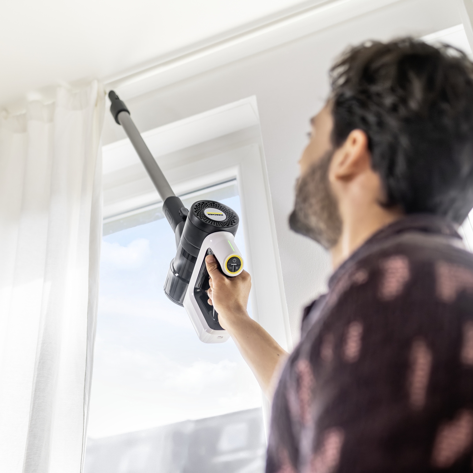 Compact design for comfortable overhead cleaning Man effortlessly vacuuming overhead along a window frame with a lightweight Kärcher battery-powered vacuum cleaner.